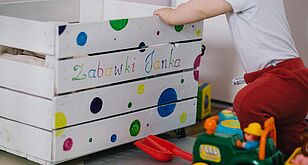 Kleinkind kniet vor einer Kiste mit Spielsachen