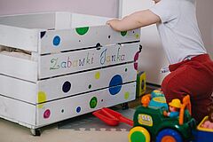 Kleinkind kniet vor einer Kiste mit Spielsachen