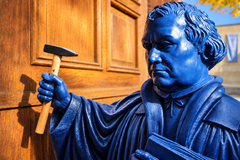 Künslticher Martim Luther hält Hammer vor schwerer Holztür